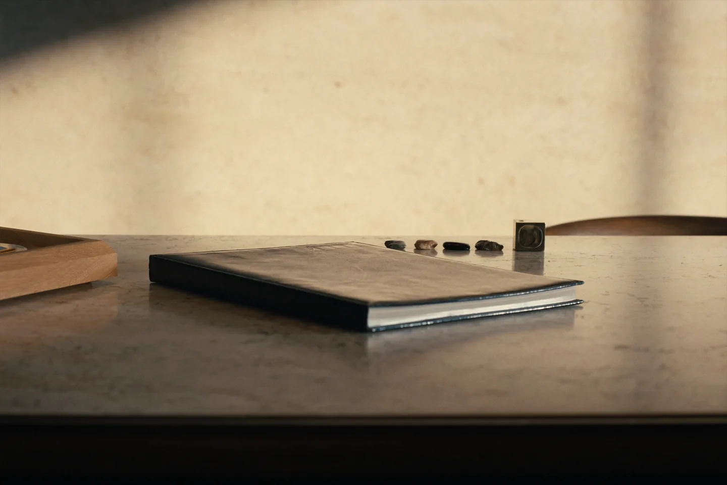 A closed leather folio and a row of natural stone samples on a warm stone desk.