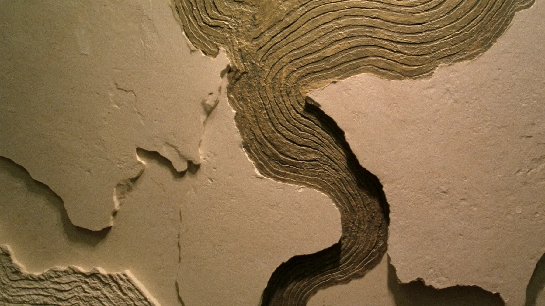 A sculptural limestone and bronze wall relief of layered topographic strata.